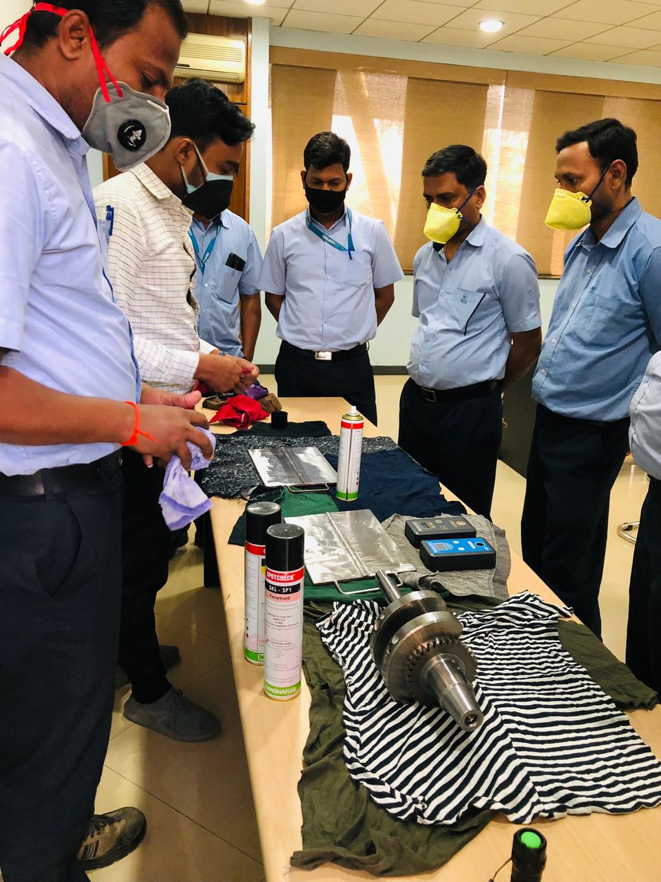 Image showing hands-on traning of employees in Liquid Penetrant Testing (LPT, PT, Dye Penetrant Testing) on an Automotive Engine Part and weld flaw specimens.