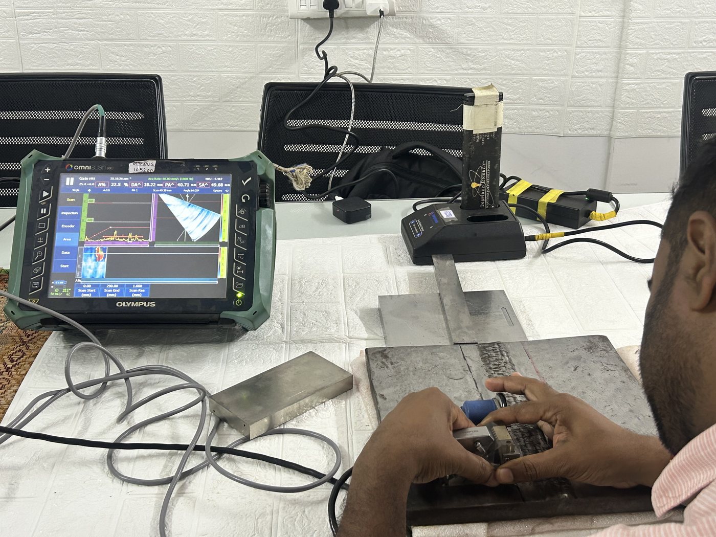 Spark NDT trainee scanning a steel weld coupon with a phased array probe on a wedge and a linear encoder, OmniScan screen showing the S-scan